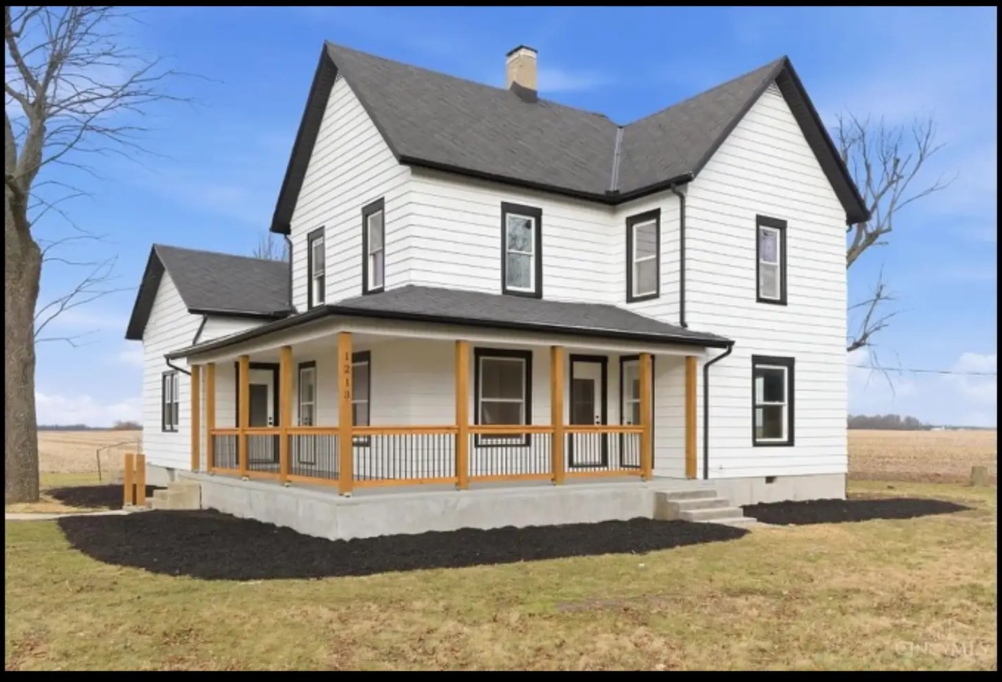 Two story white farmhouse with black trim and a wraparound porch remodeled by Green's Enterprises